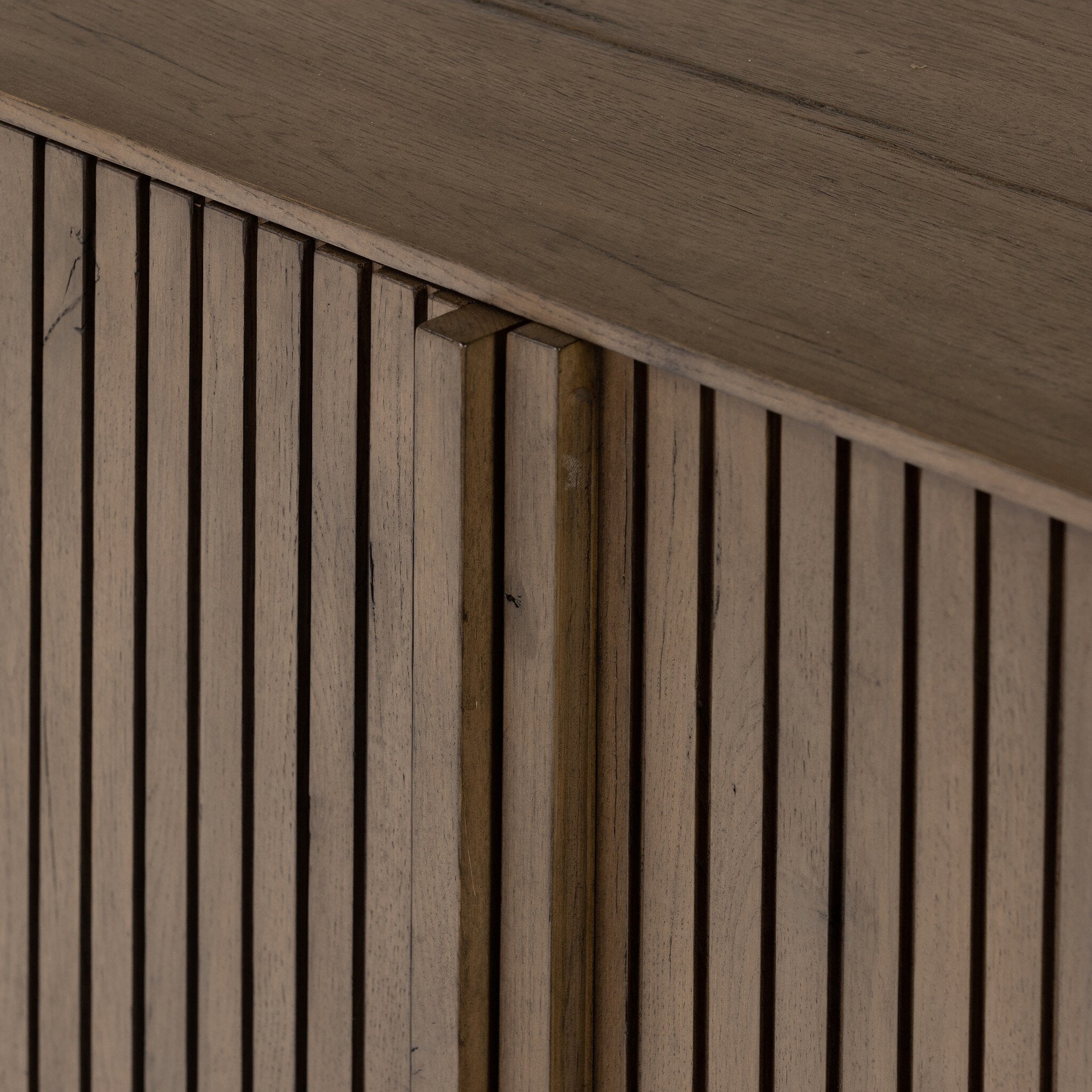 Close up of a wooden sideboard with vertical reeding on a white background.