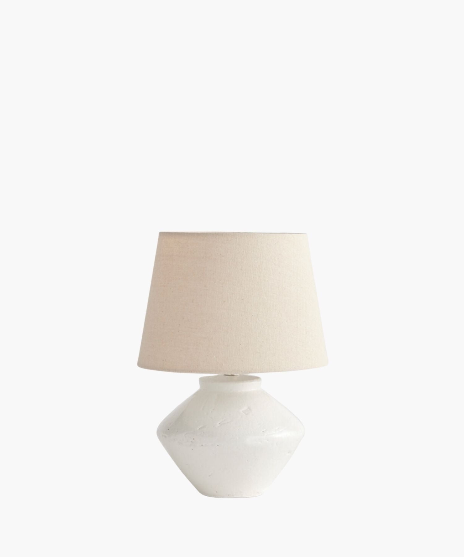A cream table lamp with a textured, wide ceramic base and a simple fabric shade. The lamp's minimalist design evokes a calm and neutral tone. | Wildwood Home Co.
