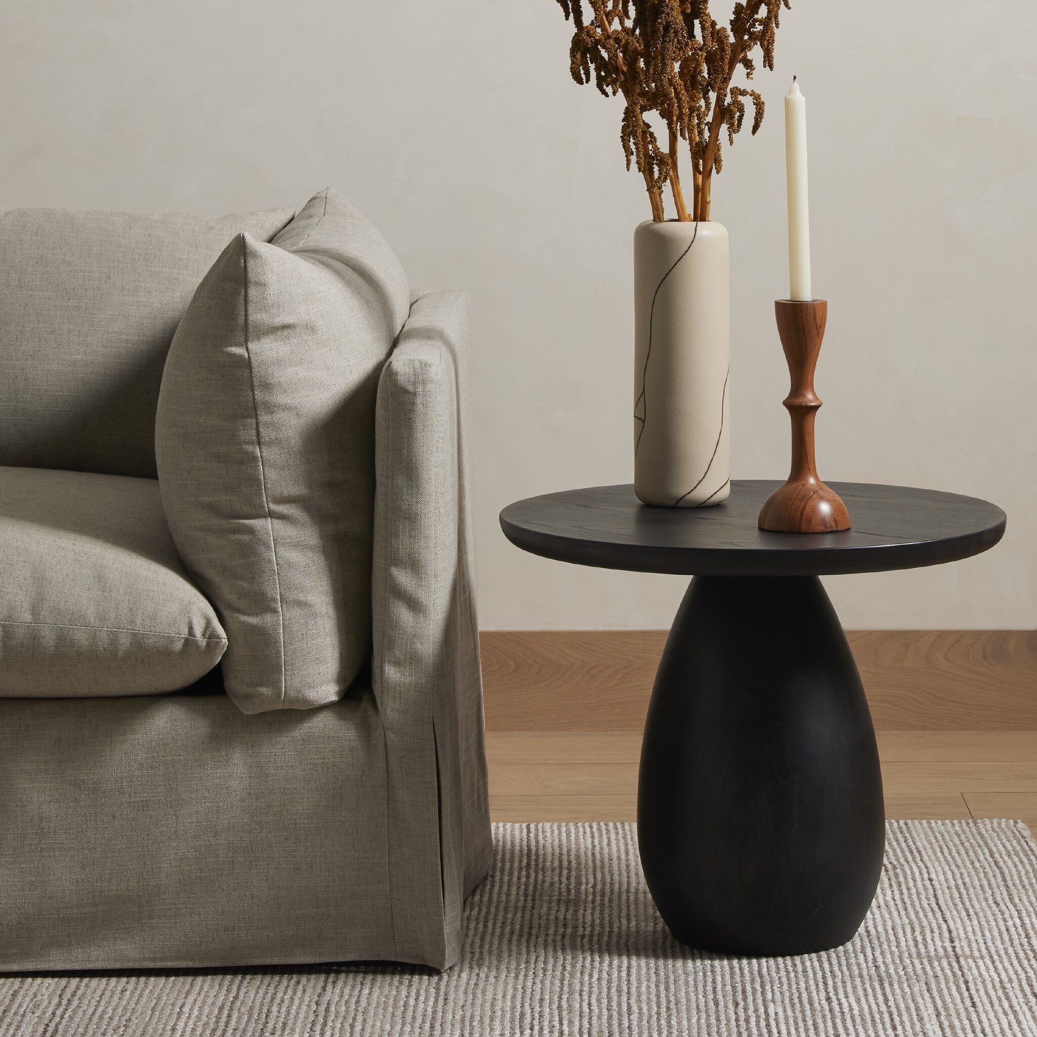 Black side table with a candle and vase next to a gray sofa in a living room. | Wildwood Home Co.
