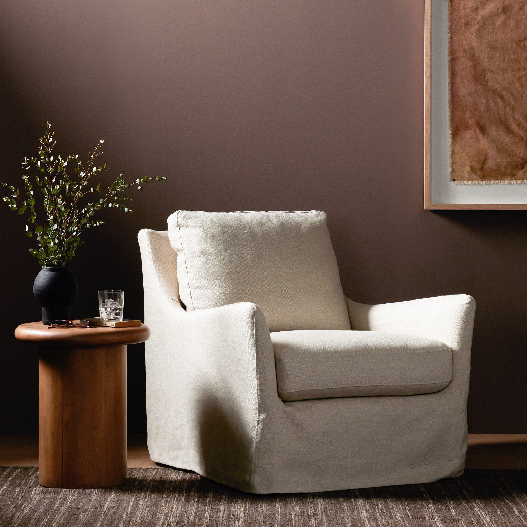 Ivory armchair in a room with a wooden side table and plant against a brown wall. | Wildwood Home Co.