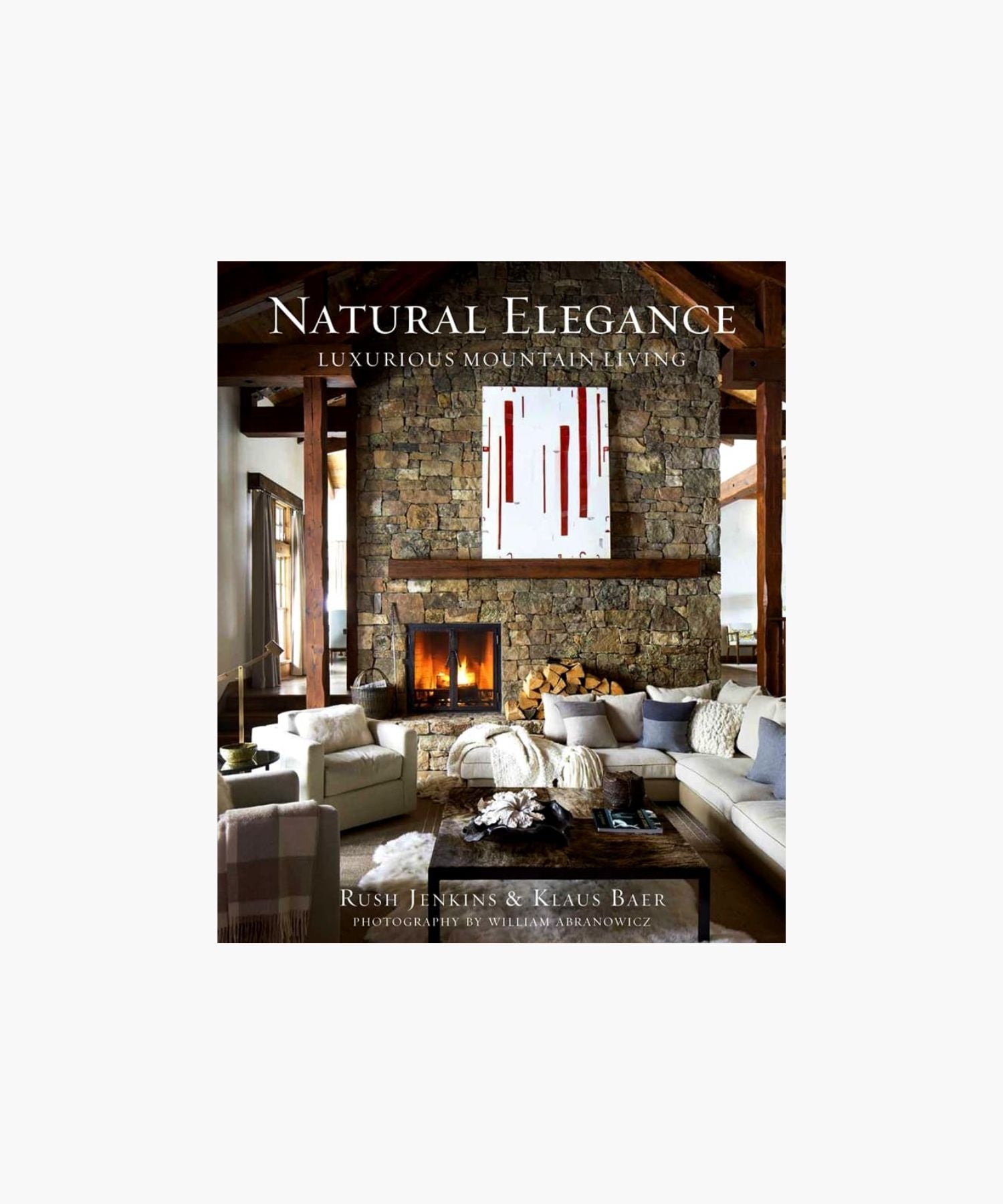 The cover of the book "Natural Elegance: Luxurious Mountain Living" by Rush Jenkins and Klaus Baer features a cozy, elegant living room features a stone fireplace, modern art, and a plush sectional. Warm tones and natural light create a welcoming, luxurious atmosphere. | Wildwood Home Co.