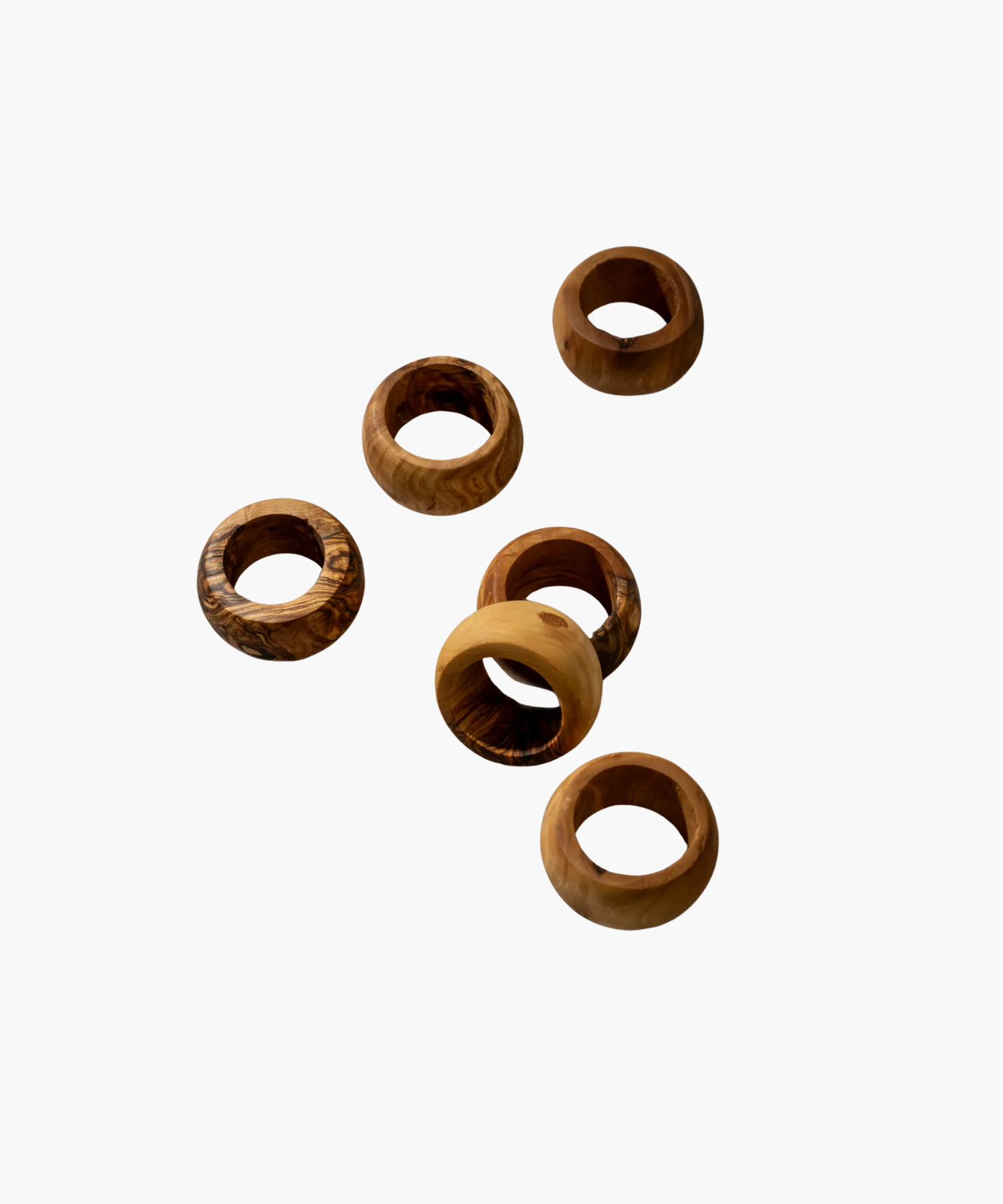 Six wooden napkin rings with varied natural grain patterns are scattered on a plain white background, showcasing a rustic and earthy aesthetic. | Wildwood Home Co.