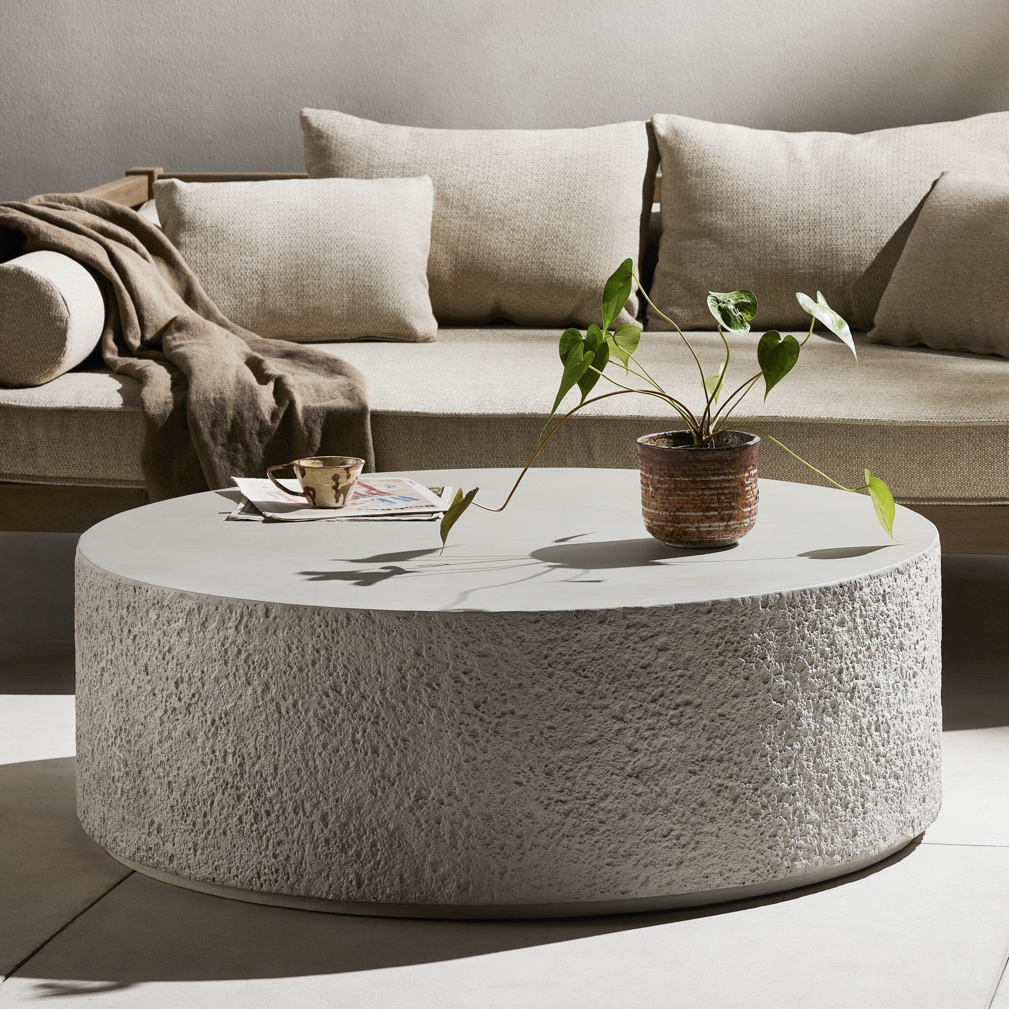 Round concrete coffee table with a plant and cup in front of a beige sectional sofa. | Wildwood Home Co.