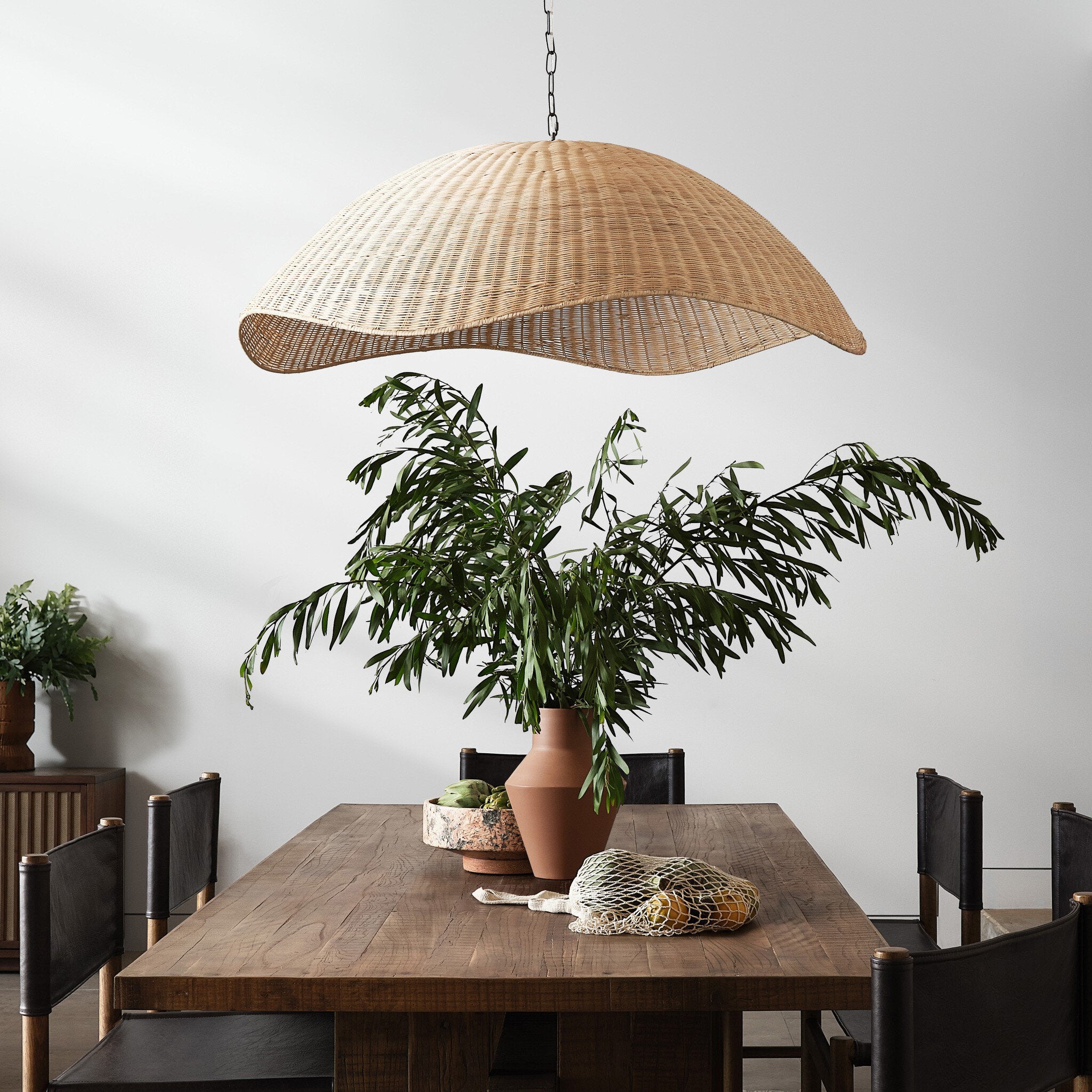 Dining area with a woven pendant light over a  wooden table, and potted plants. | Wildwood Home Co.