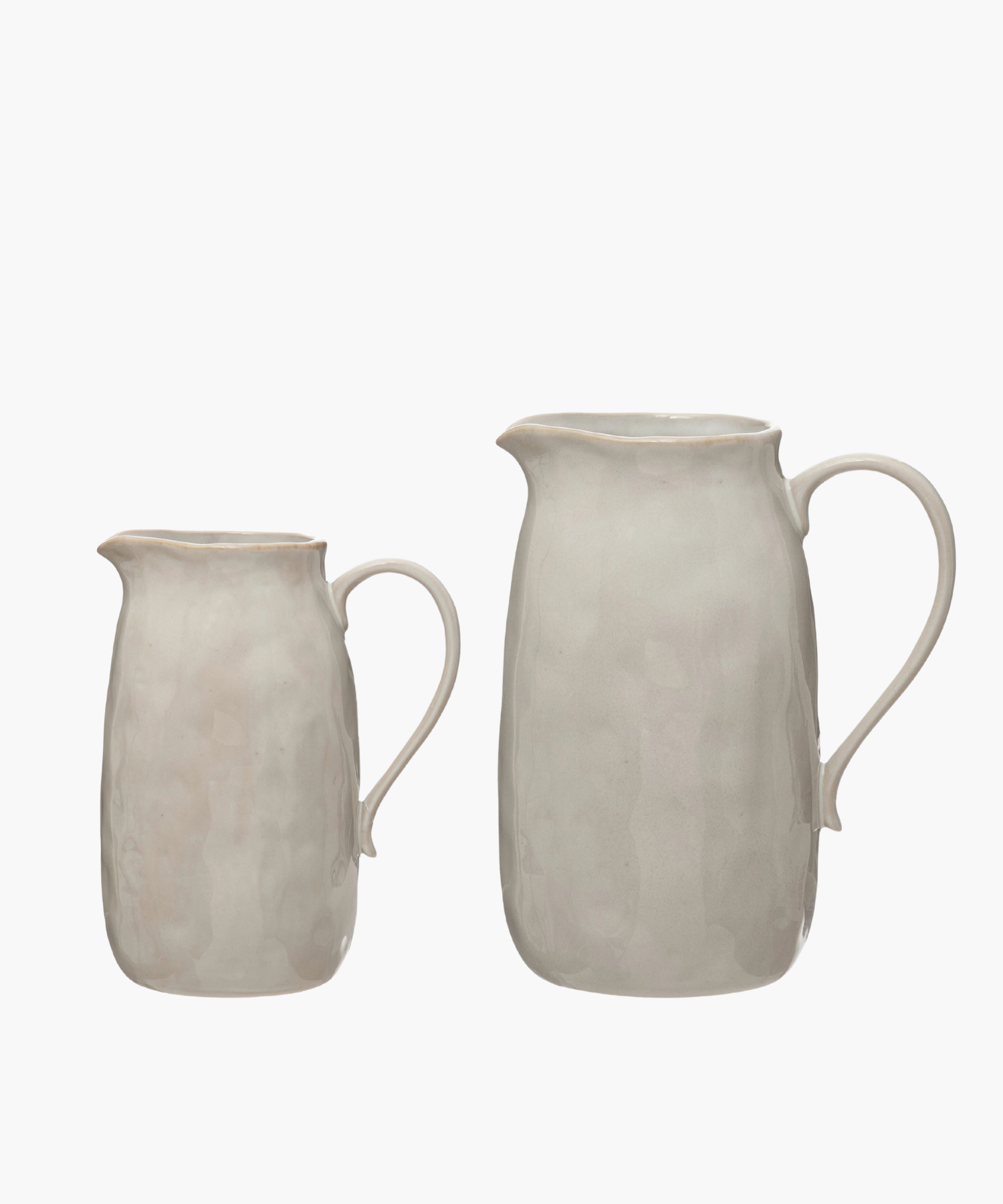Two simple, elegant beige ceramic pitchers in various sizes with a smooth curved handle and a subtly textured surface, evoking a minimalist and classic design. | Wildwood Home Co.
