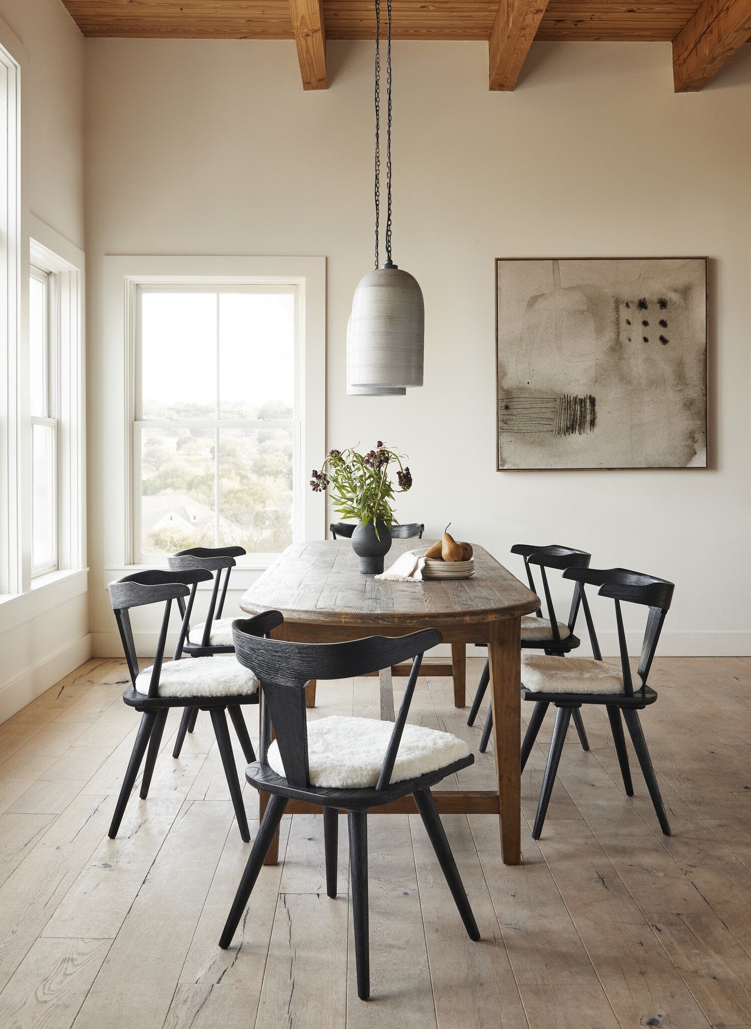 Dining room with wooden table and black chairs, pendant light, and abstract painting. | Wildwood Home Co.