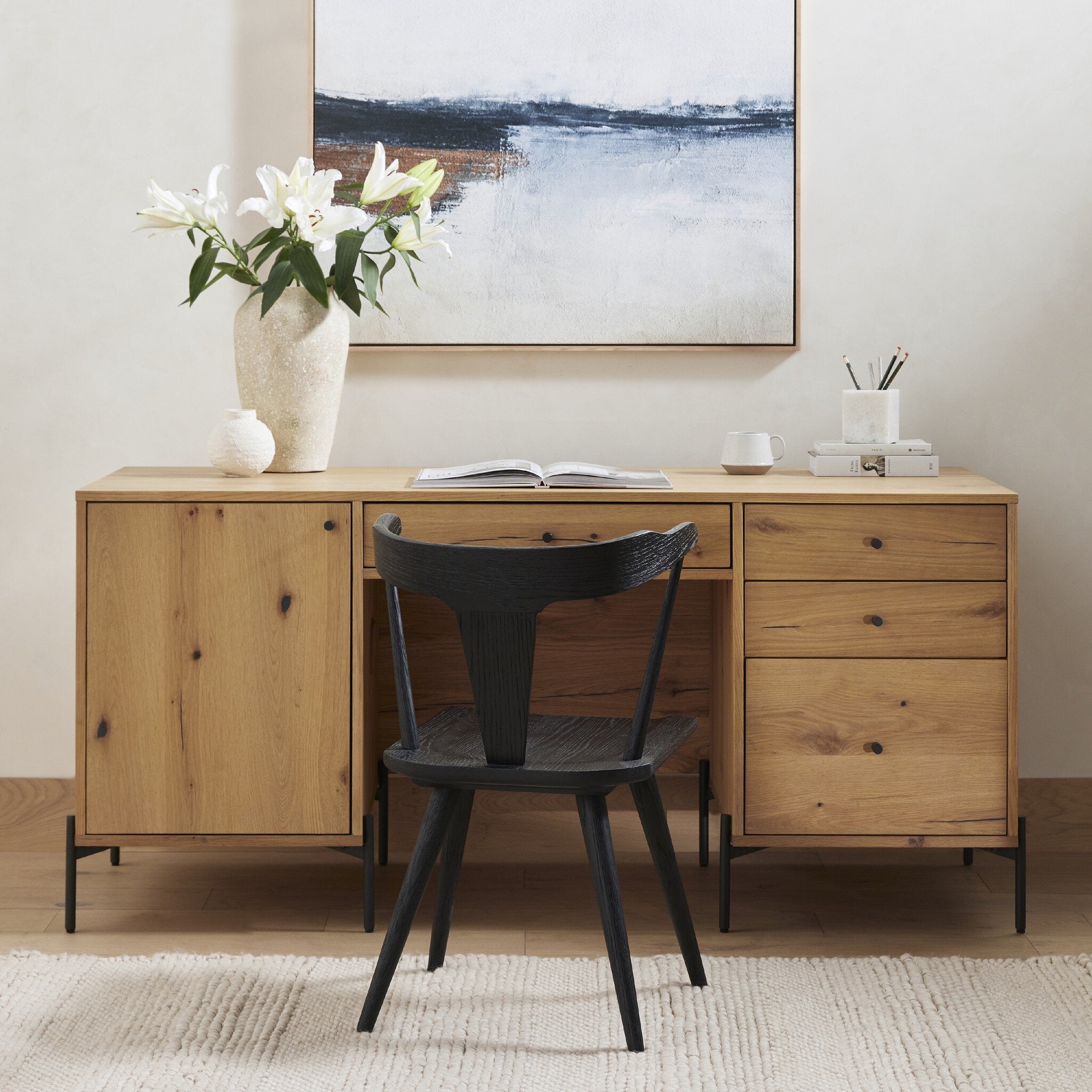 Wooden desk with black chair, vase with flowers, and abstract painting in a room.