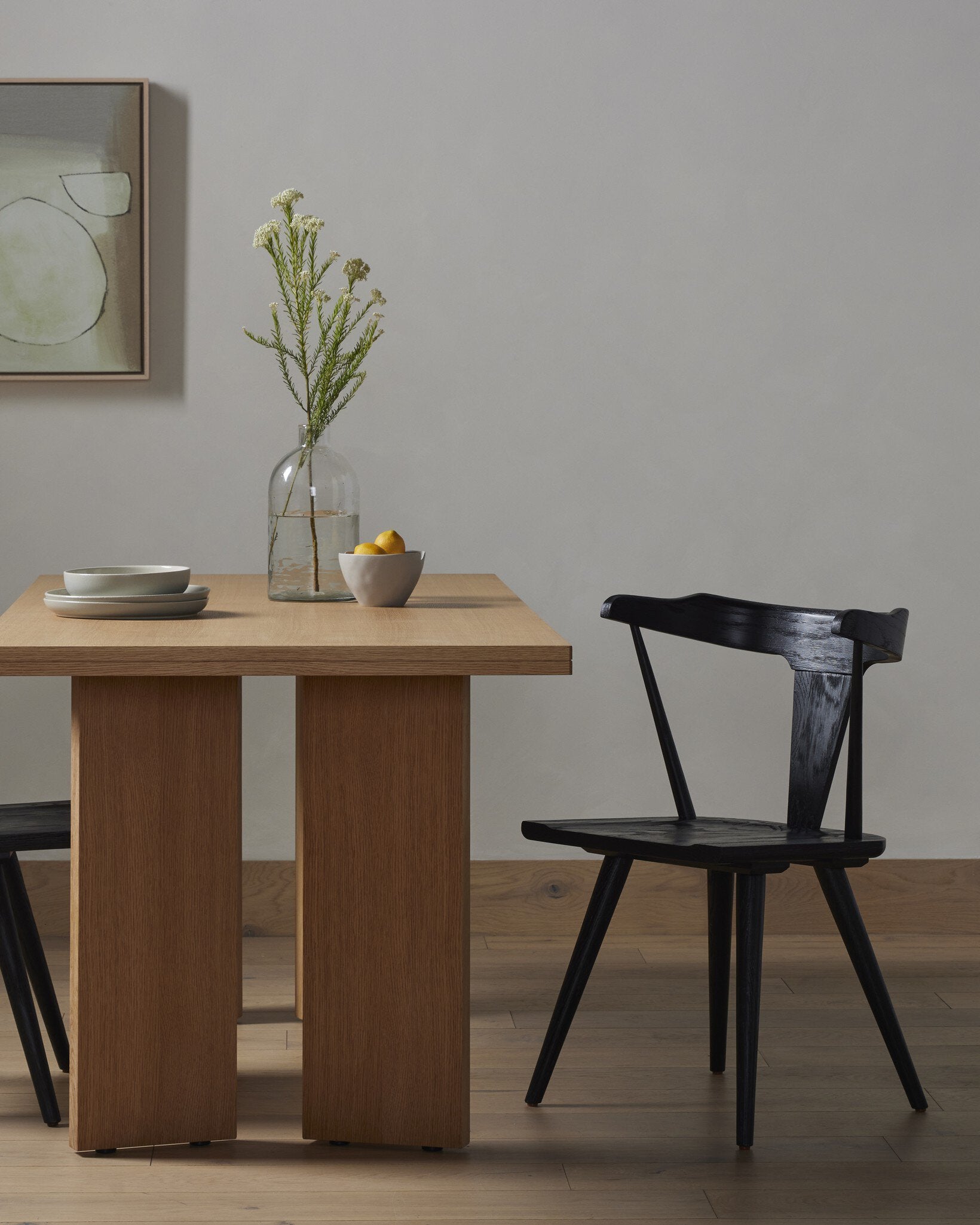 Wooden dining table with a black chair against a plain wall