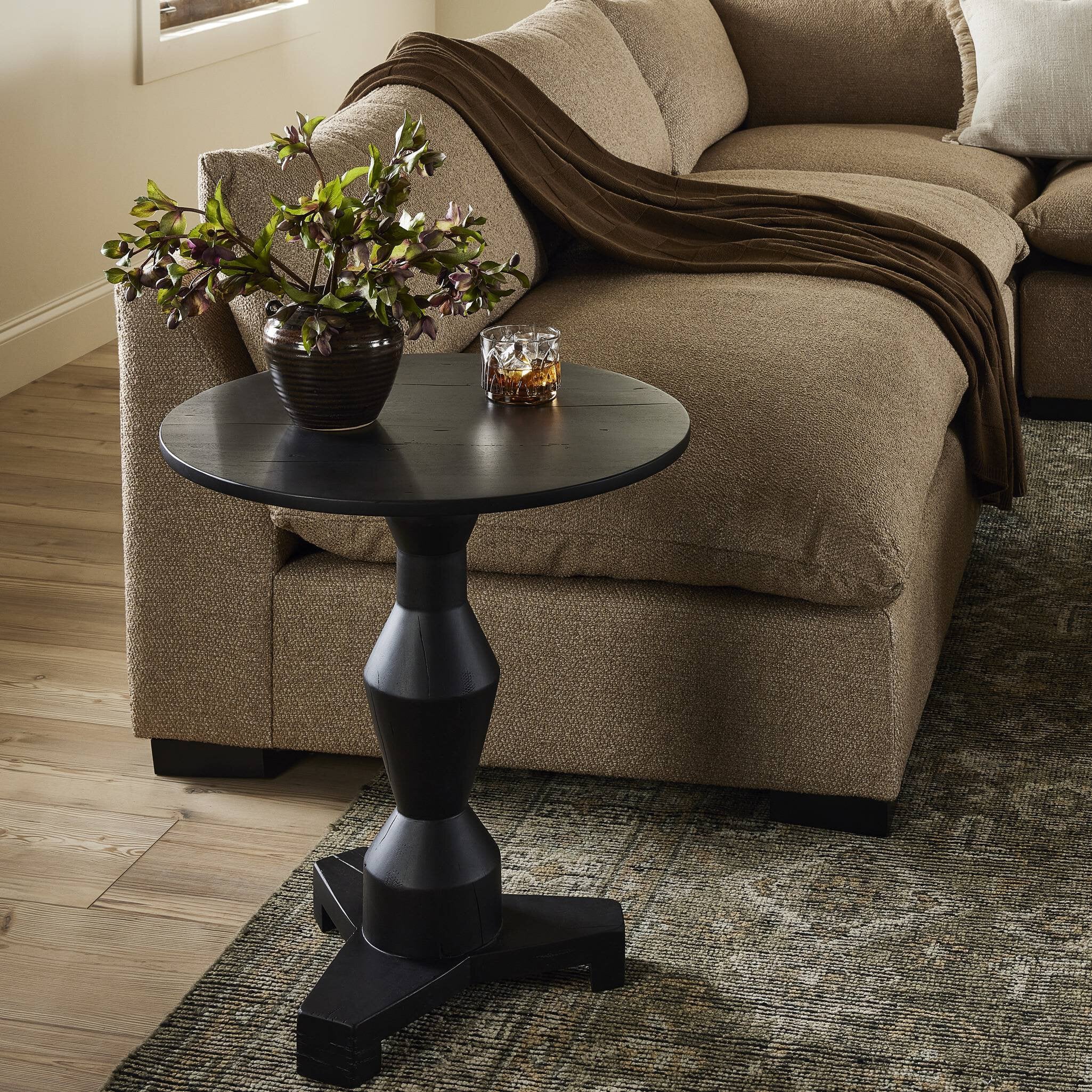 Black side table with a plant and glasses next to a beige sofa in a living room. | Wildwood Home Co.