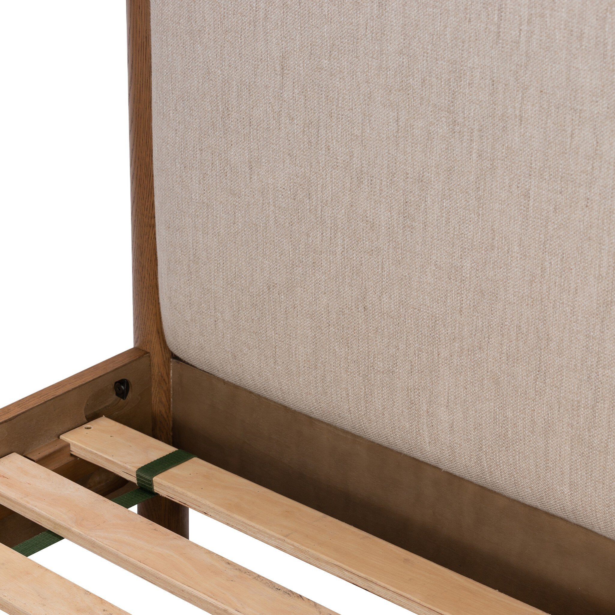 Close up of a wooden bed with upholstered headboard and white bedding on a white background.