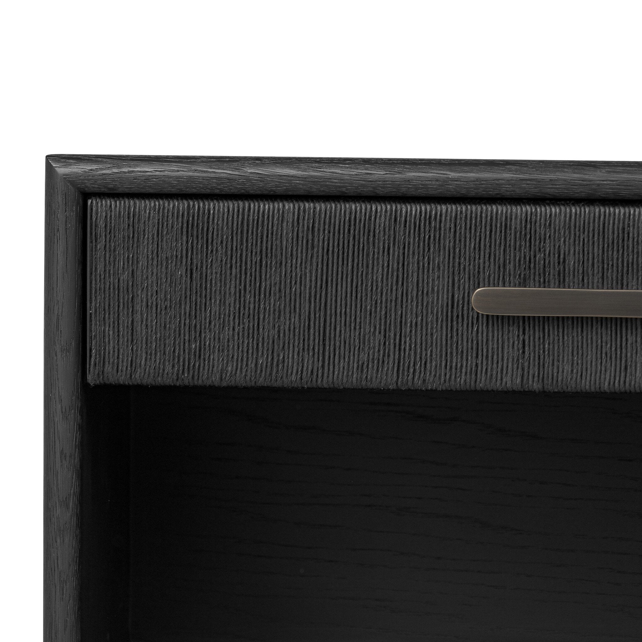 Close up of a black-finished oak nightstand with a smooth top and single drawer front of woven paper on a white background. 