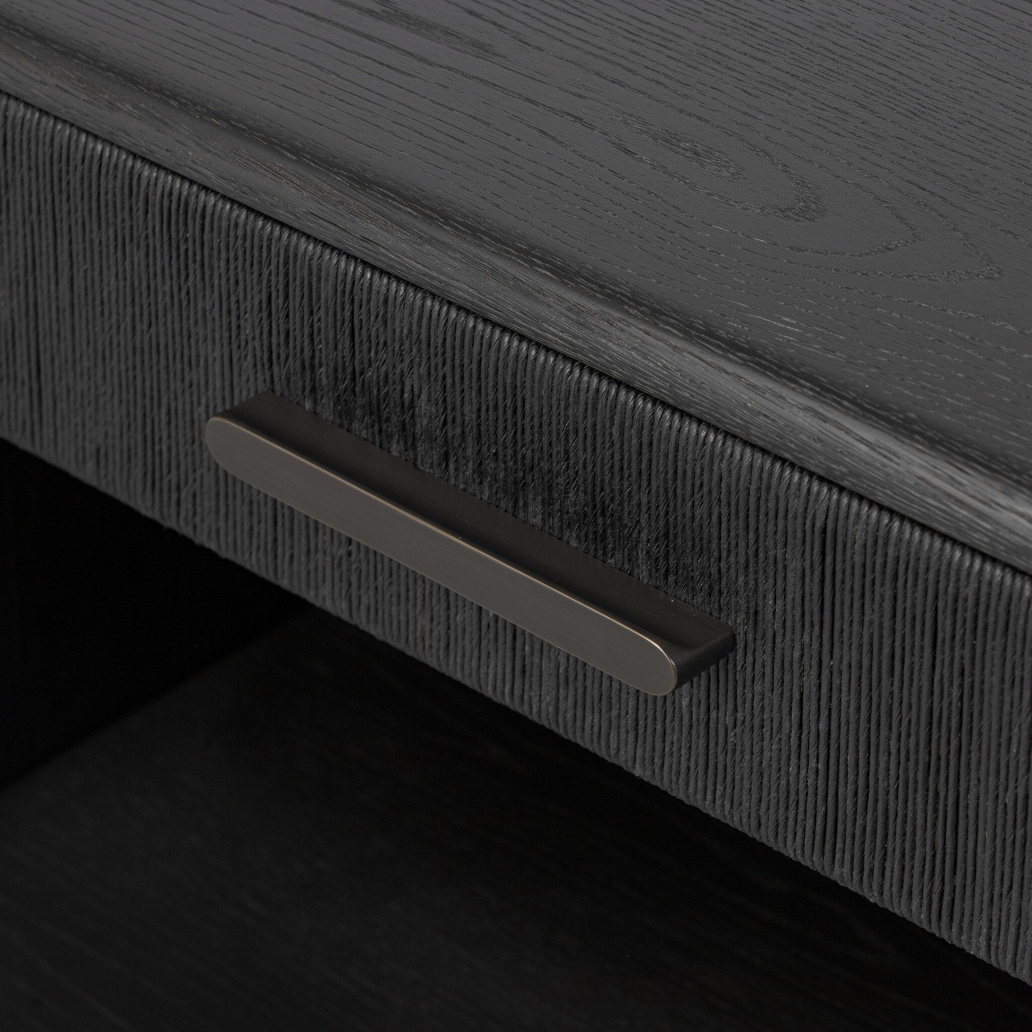 Close up of a black-finished oak nightstand with a smooth top and single drawer front of woven paper on a white background. 