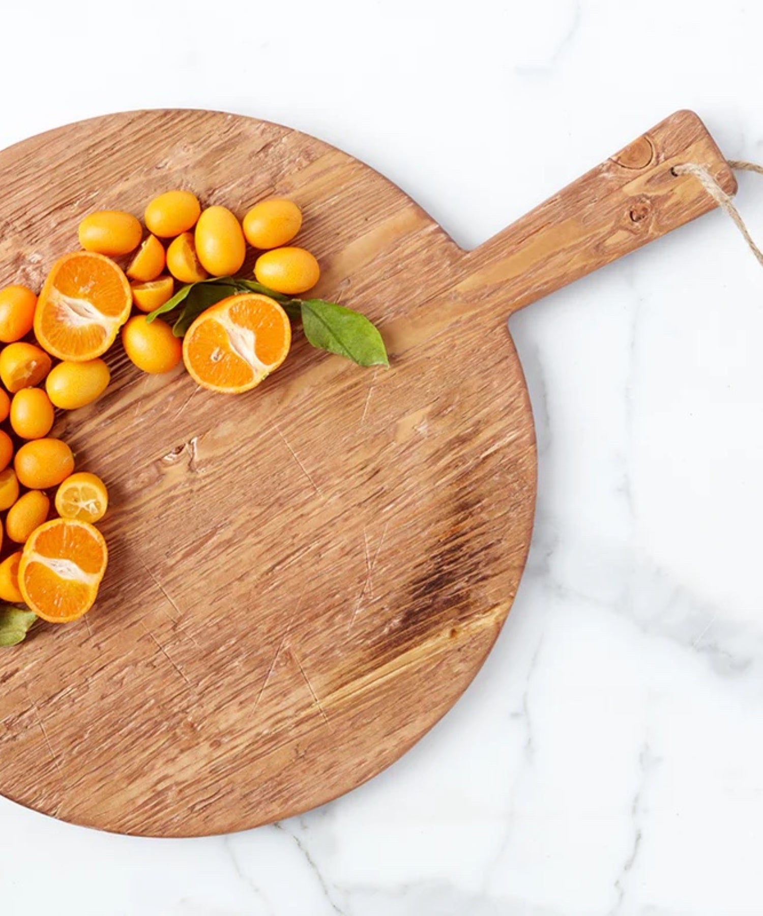A round pine wood cutting board with a smooth surface and natural grain. It has a handle with a rope loop for hanging, conveying a rustic charm styled with sliced oranges. 
