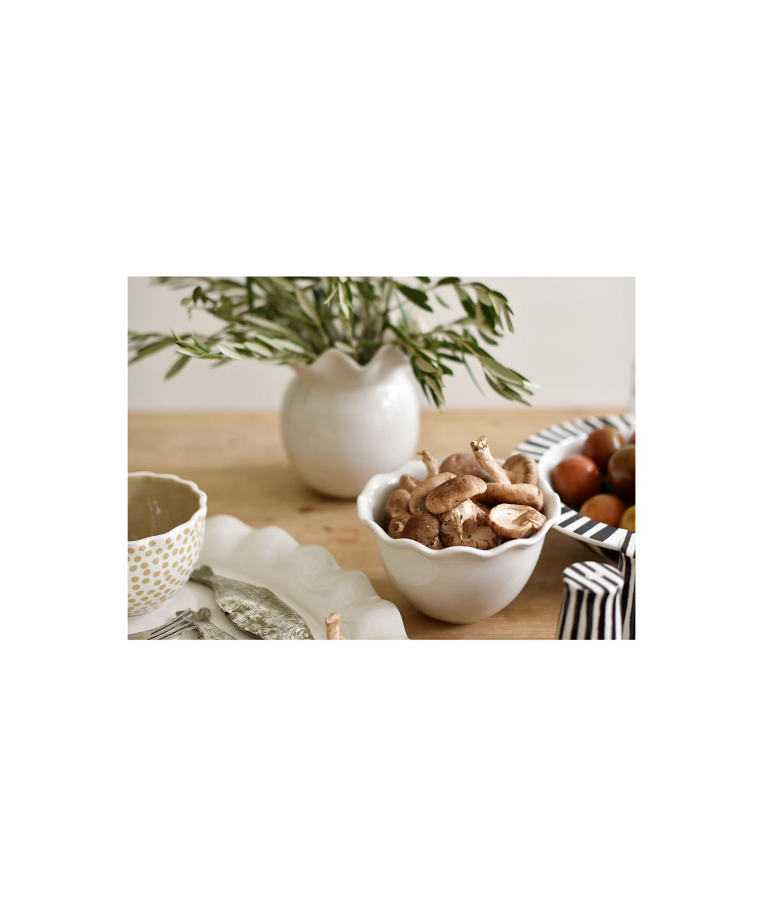 White ceramic vase with a glossy finish and wavy, ruffled rim styled on a table with greenery. The vase has a round, bulbous body, conveying elegance and simplicity. | Wildwood Home Co.