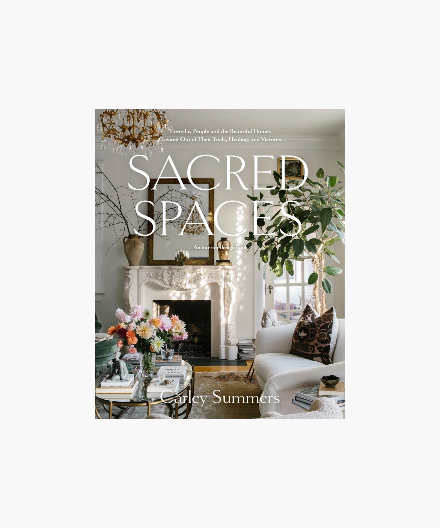 The cover of the book "Sacred Spaces" by Carley Summers featuring a cozy living room with elegant decor; a white fireplace, chandelier, vibrant flowers, and lush greenery create a tranquil, inviting ambiance. | Wildwood Home Co.