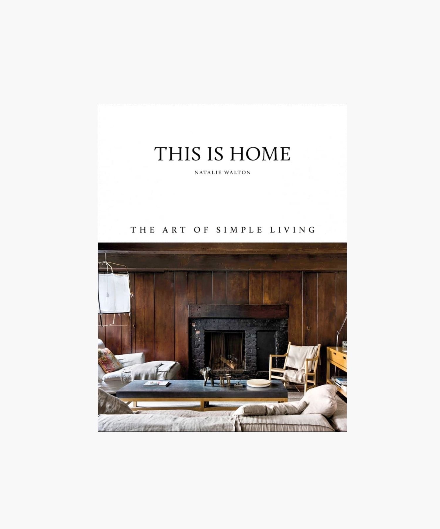 Cover of the book "This Is Home" by Natalie Walton, featuring a rustic, cozy living room with wooden walls, a fireplace, seating, and a coffee table. | Wildwood Home Co.