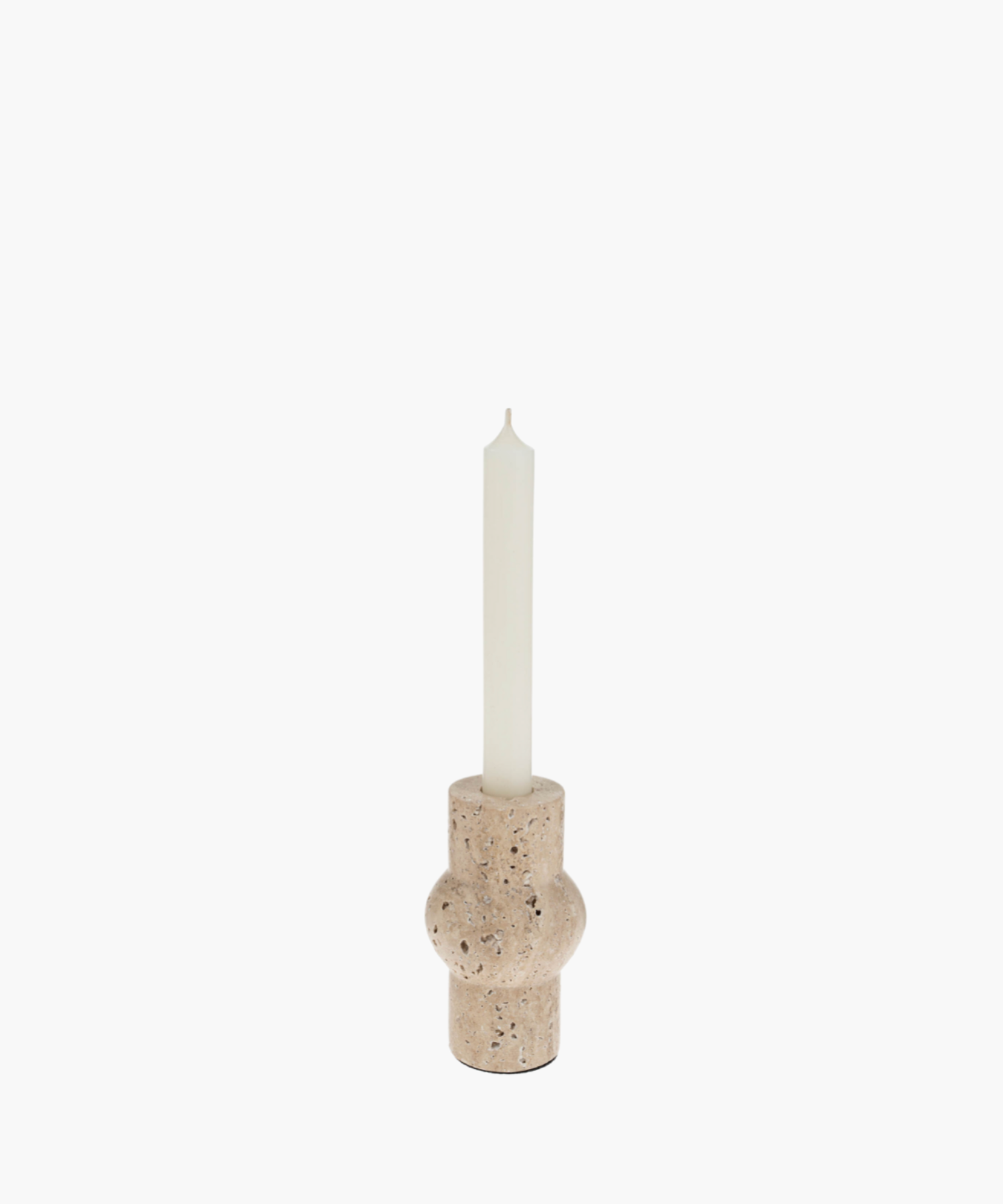 A tall white candle in a rounded, beige travertine stone holder with a textured surface. The minimalist design evokes a calm and serene atmosphere.