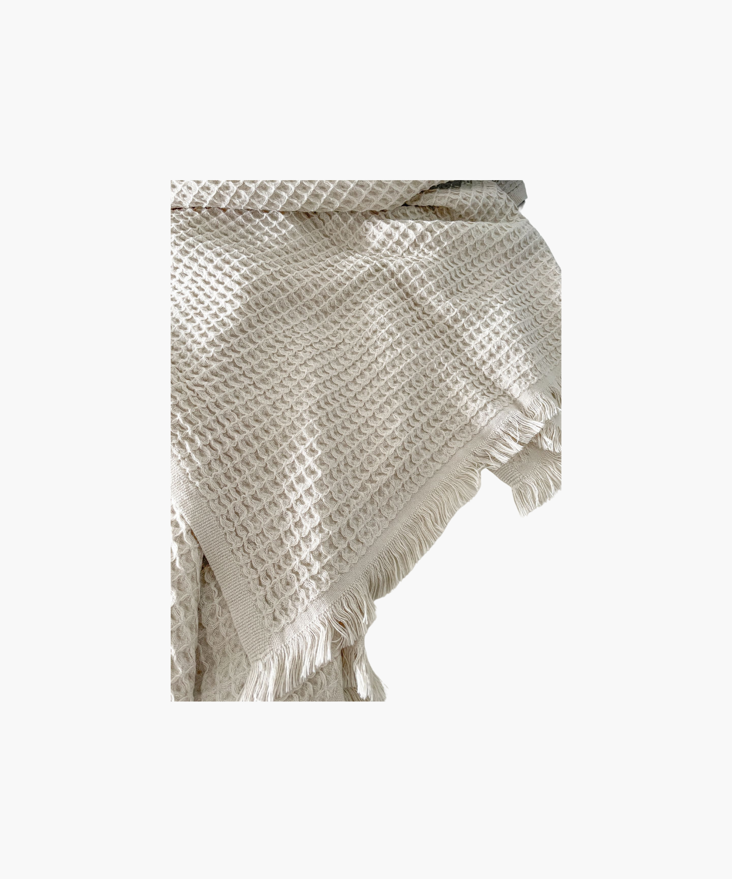 Beige waffle-textured throw blanket with fringed edges, laid flat. The soft material conveys a cozy, inviting feel. Suitable for any living room or bedroom.
