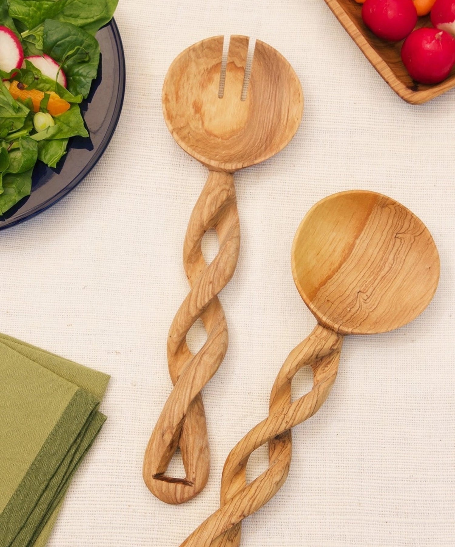 Two ornately carved olive wood salad servers, a spoon and a fork, featuring twisting handles and rich natural wood patterns. They convey a rustic, artistic feel. | Wildwood Home Co.