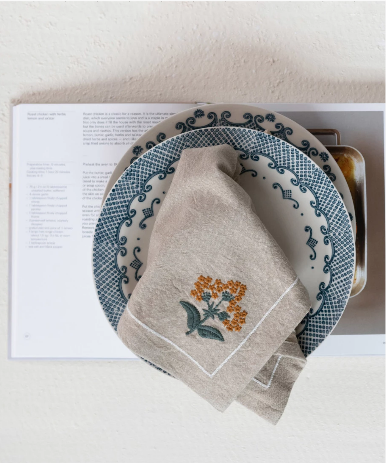 A beige cloth napkin with orange floral embroidery folded open on a plate, suggesting elegance and simplicity. | Wildwood Home Co.