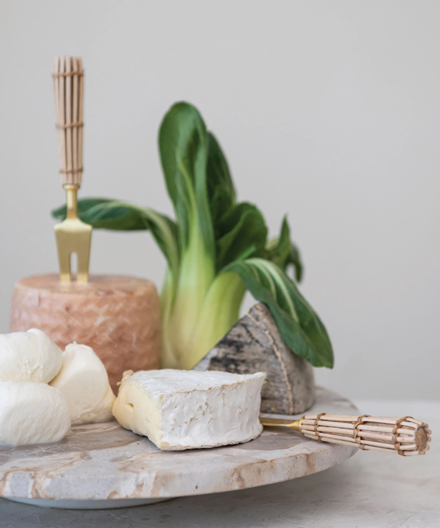 A round marble lazy susan with a smooth, polished surface featuring gray and beige veining styled with cheeses and cheese knives. | Wildwood Home Co.